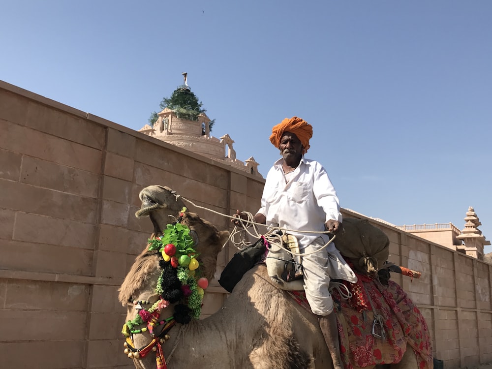 man in white robe riding on brown horse during daytime