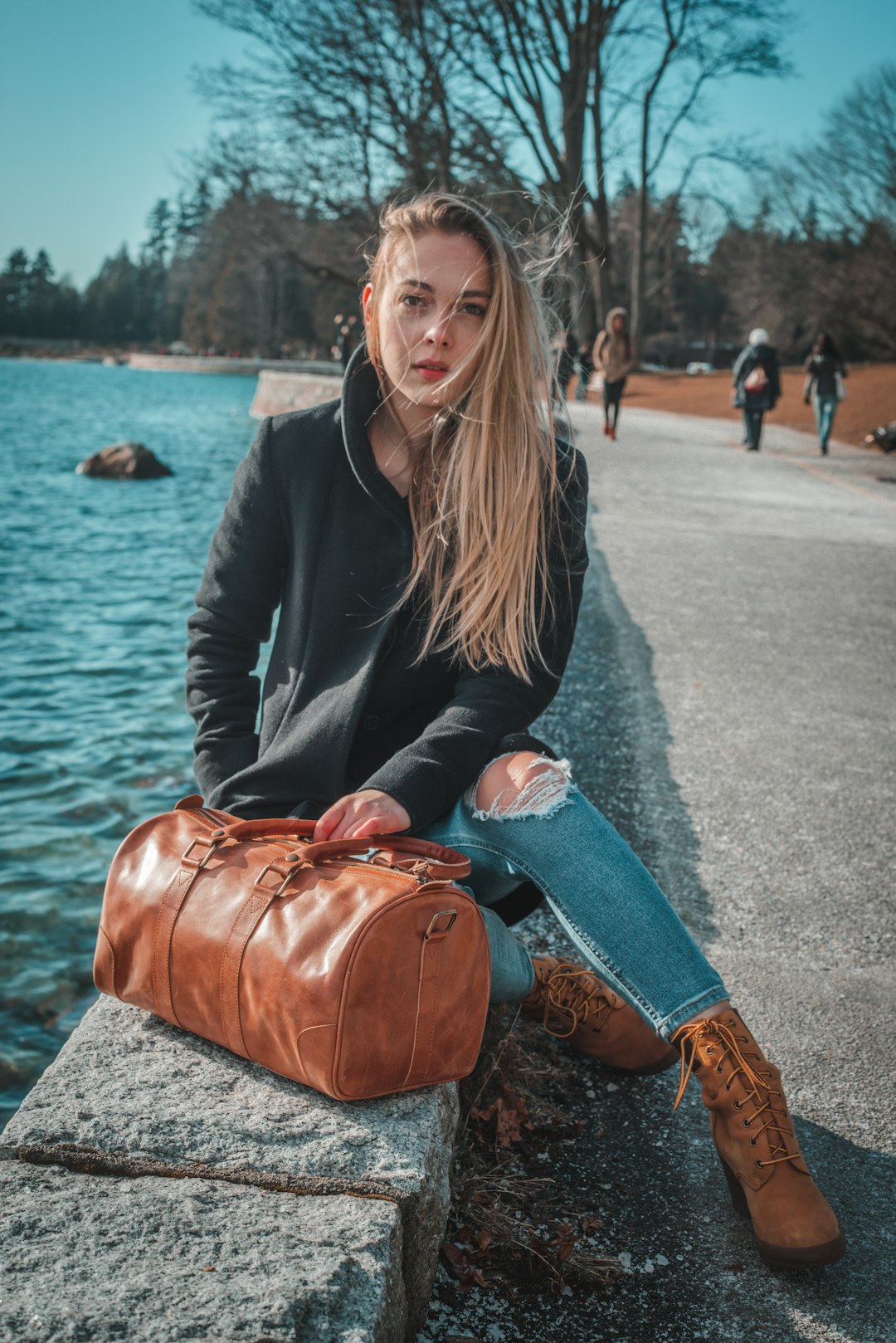 woman in black jacket and blue denim jeans sitting on gray concrete bench during daytime