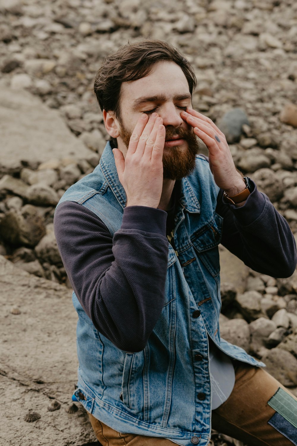 man in blue denim jacket covering his face with his hand