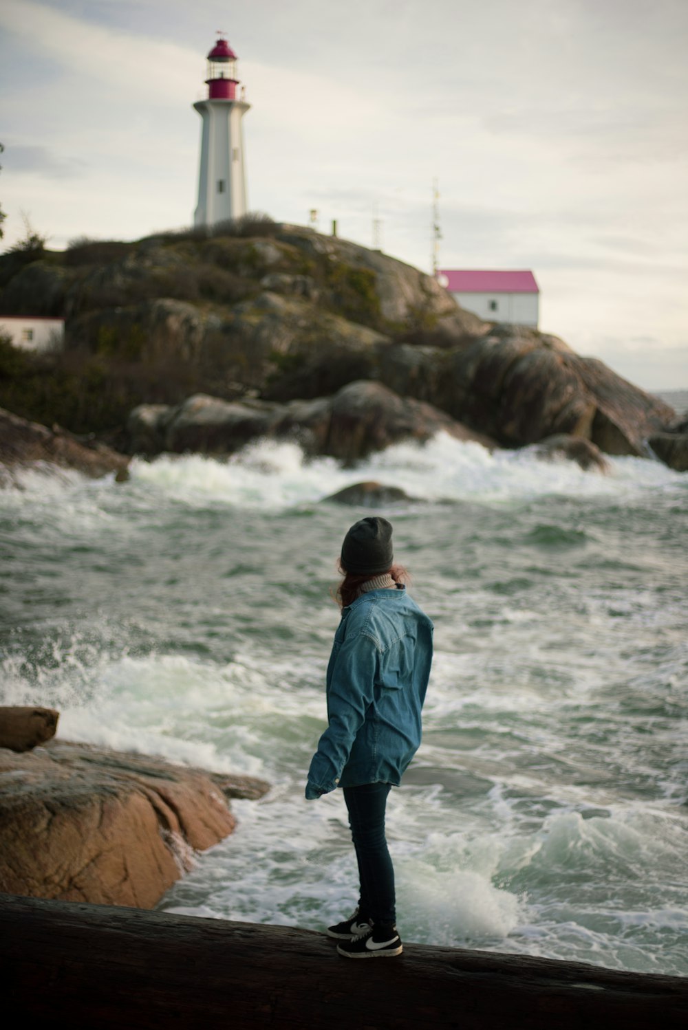 man in blue jacket standing on brown rock near body of water during daytime