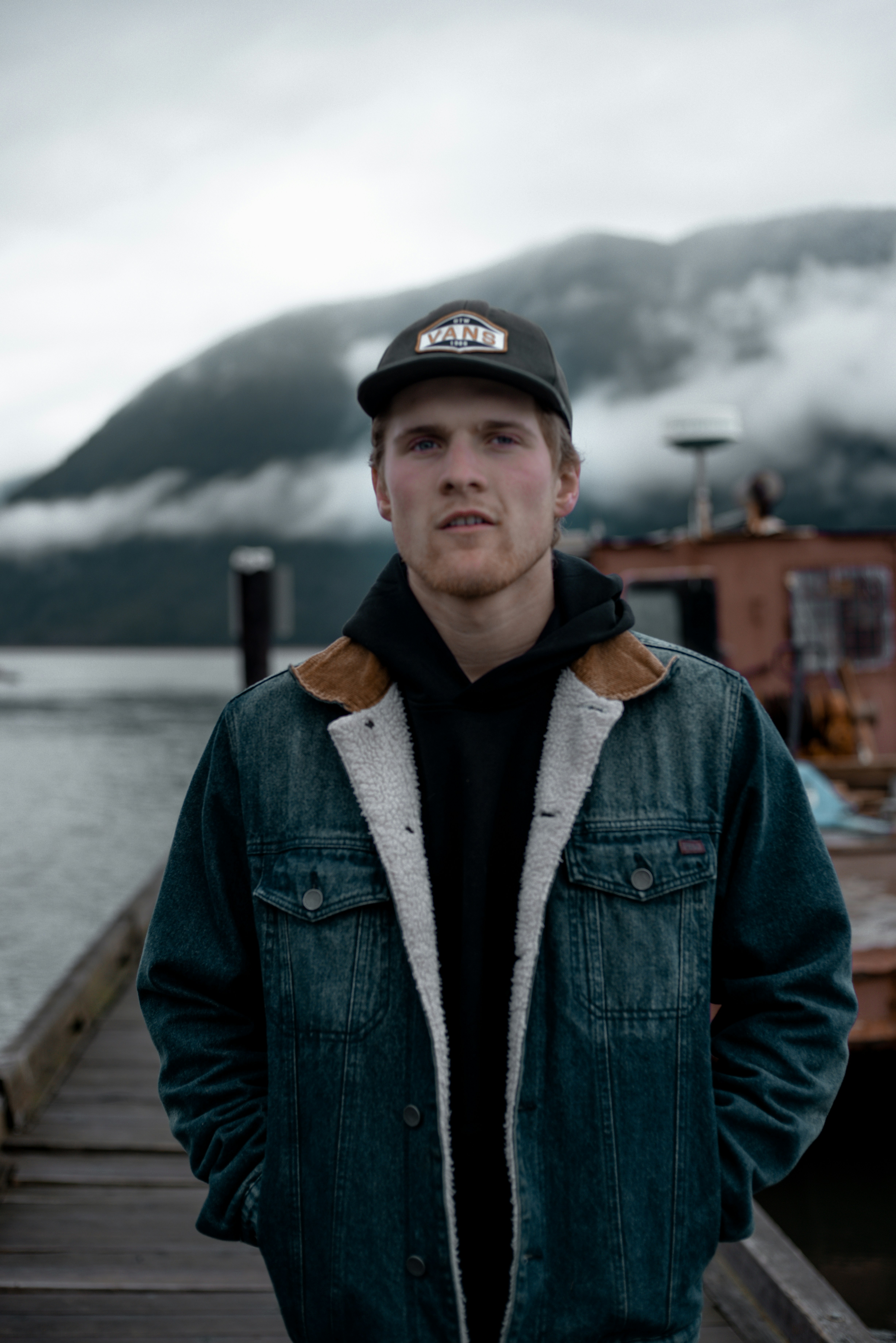 Man in blue denim jacket and black cap standing on wooden dock