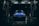 A blue car with raindrops is parked inside an illuminated car wash bay during nighttime. The scene is dark with light reflecting off the wet surfaces, creating a dramatic and moody atmosphere. The car wash bay has visible signage and equipment surrounding the vehicle.