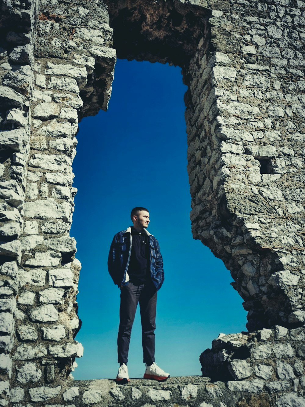 man in black jacket standing on gray concrete wall during daytime