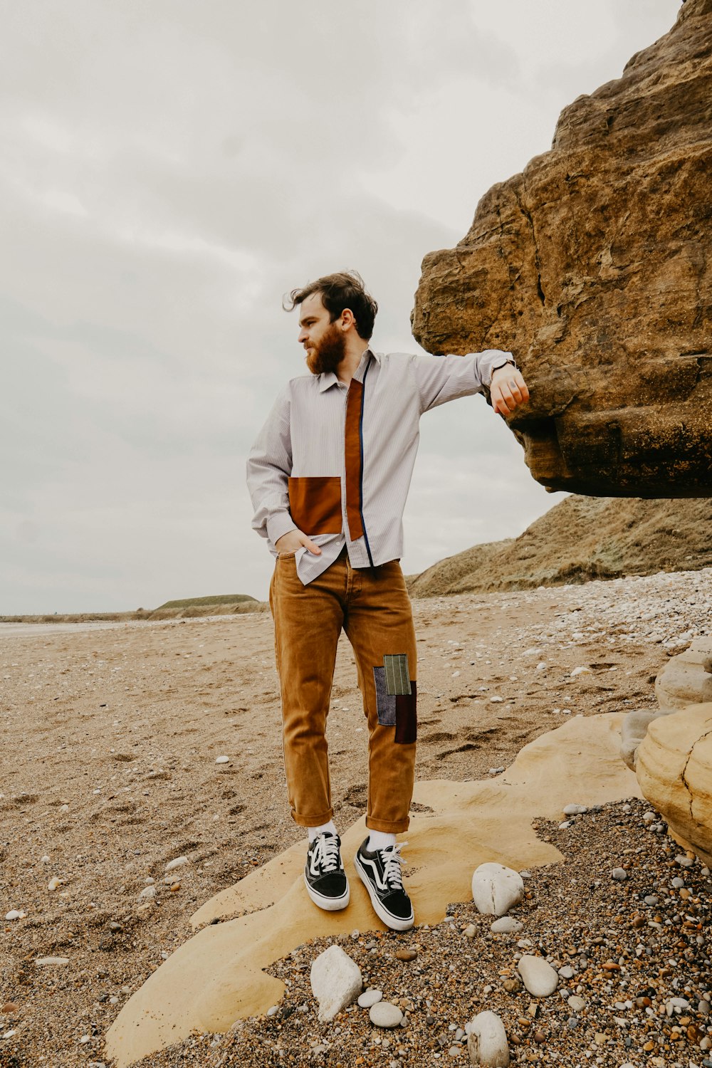 man in white dress shirt and brown pants standing on brown rock during daytime