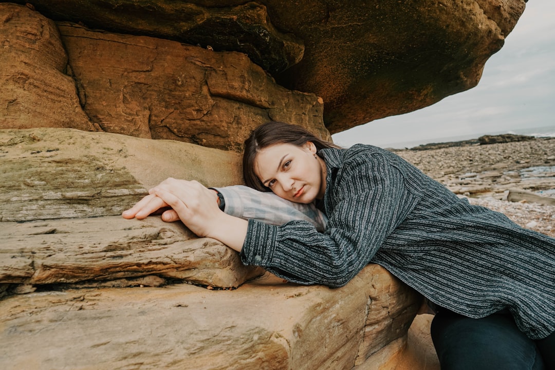 woman in gray and black stripe long sleeve shirt lying on brown rock