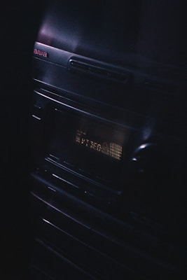 A vintage audio stereo system with a display screen showing text, illuminated in a dimly lit environment. The brand name Aiwa is visible at the top left corner, and the equipment has a sleek, reflective surface with buttons and a knob.