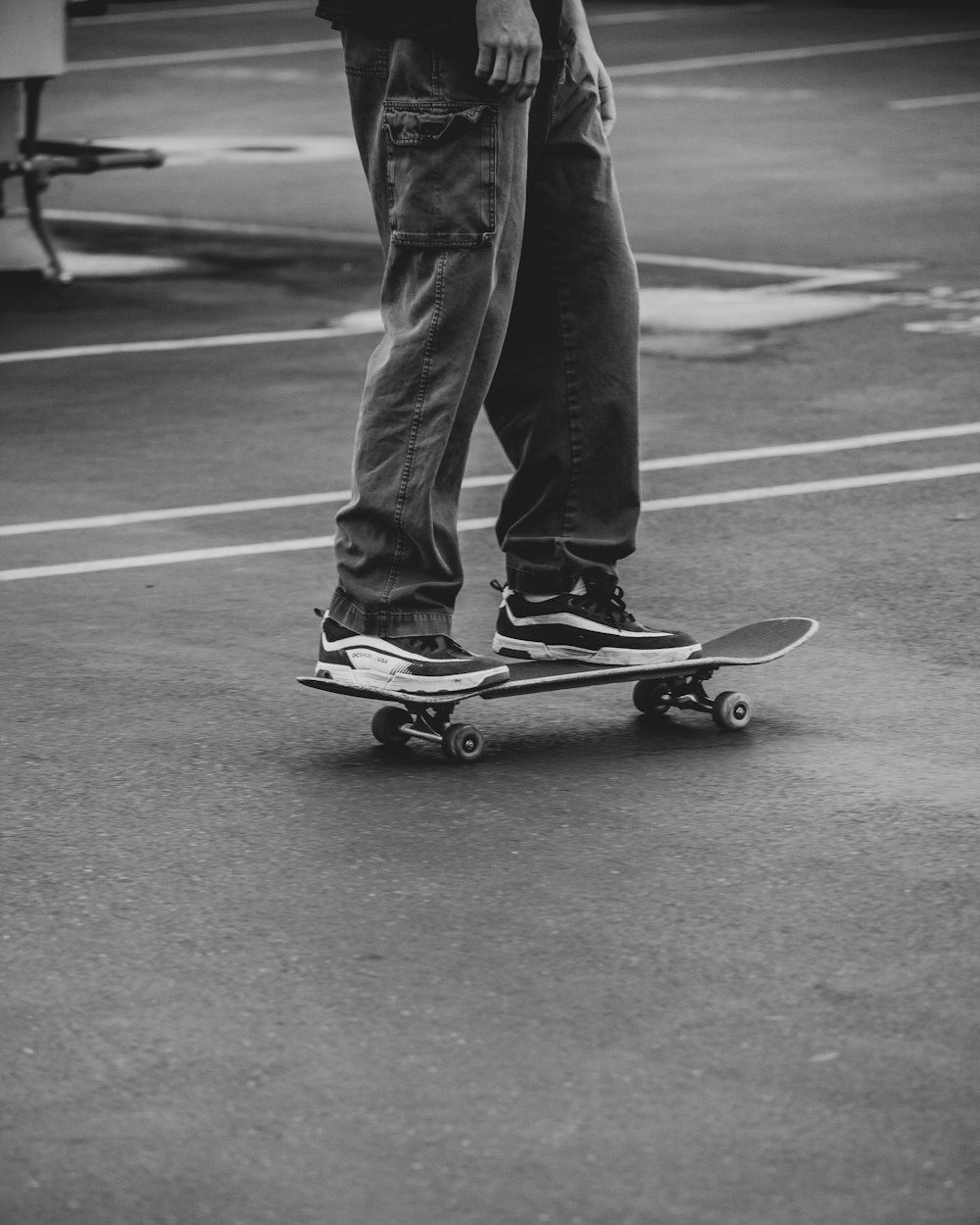 Mann in schwarzen Hosen und schwarzen Turnschuhen fährt tagsüber auf dem Skateboard auf grauer Betonstraße