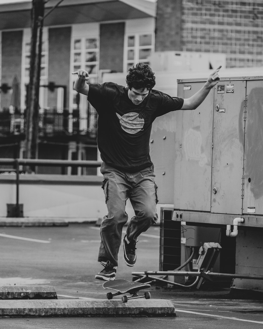 Mann in schwarzem T-Shirt und brauner Hose springt auf Skateboard in Graustufenfotografie