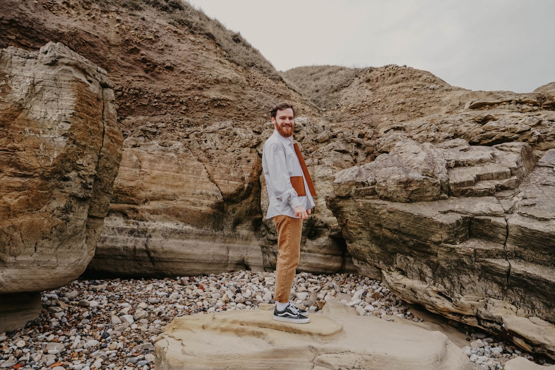 man in white dress shirt standing on brown rock formation during daytime