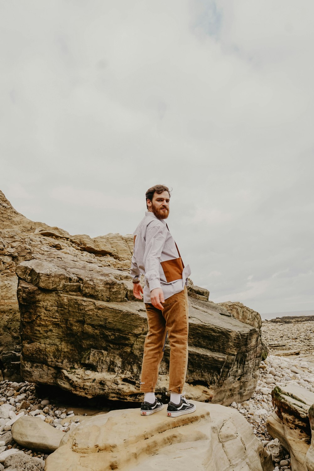 man in white dress shirt and brown pants standing on brown rock formation during daytime