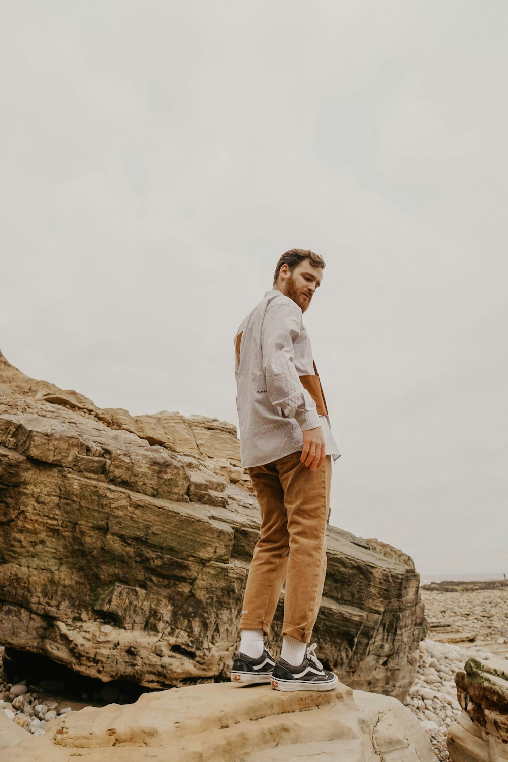 man in white dress shirt and brown pants standing on brown rock formation during daytime