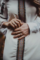 A close-up of hands adorned with colorful noorzar rings resting on a traditional embroidered cloth.