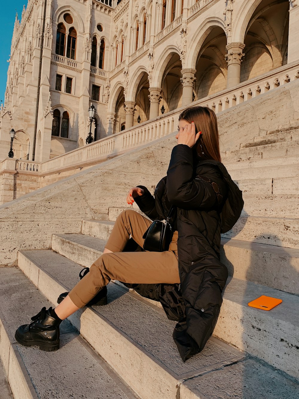 woman in brown coat and brown pants sitting on concrete bench during daytime