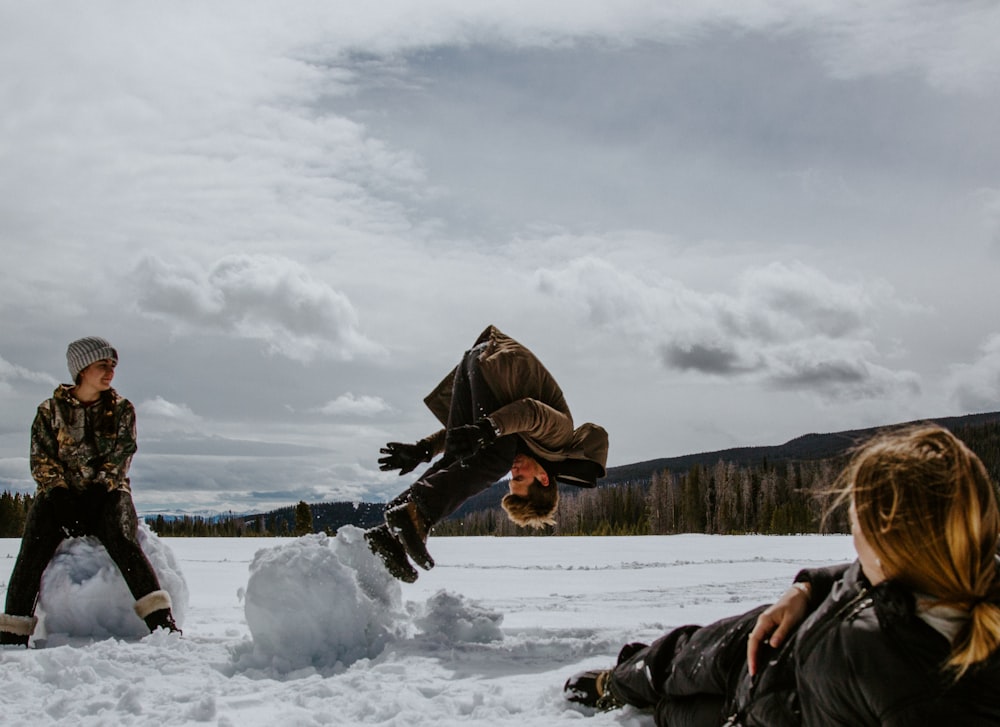 person in black jacket and brown pants lying on snow covered ground during daytime