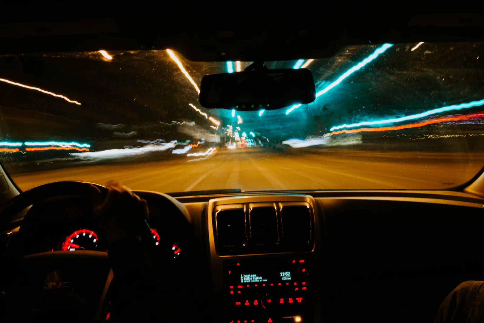 Vista desde el interior de un vehículo circulando de noche por una vía urbana iluminada