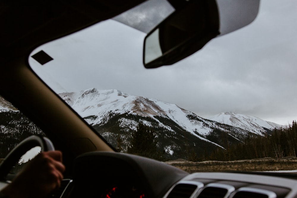 person driving car on road near snow covered mountain during daytime