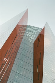 A modern architectural structure featuring sharp, angular lines and glass surfaces reflecting the sky. The building has red and grey panels with a prominent Canadian flag displayed.