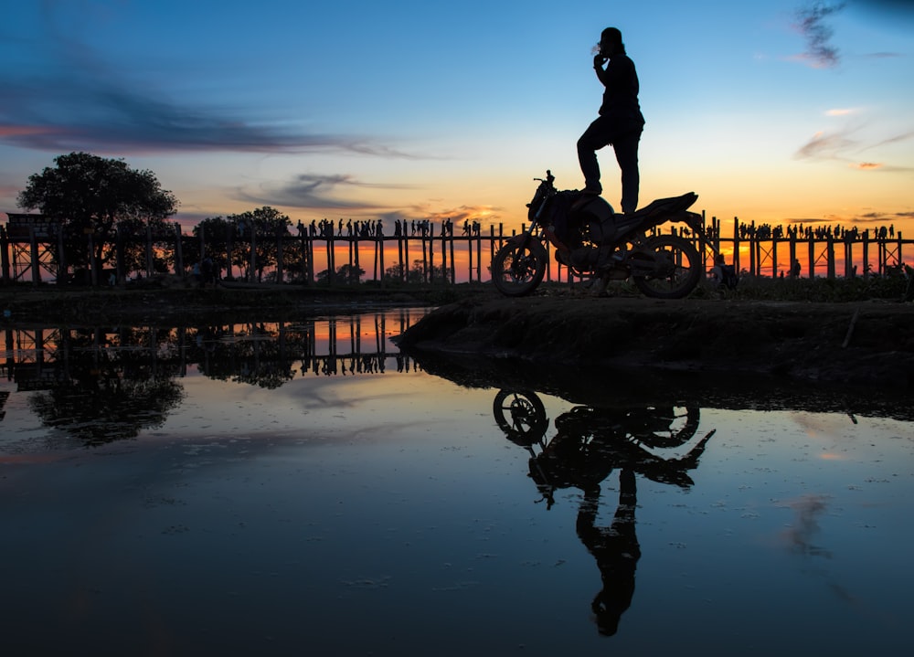 silhouette of man riding motorcycle on water during sunset