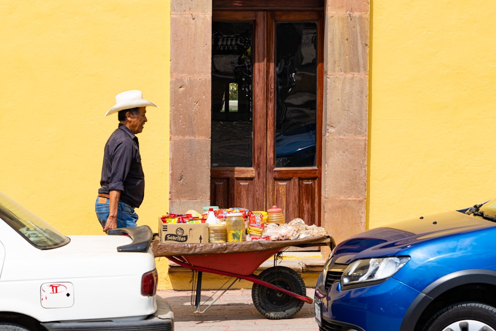 昼間、茶色の木製のドアのそばに立つ青いドレスシャツと茶色の帽子をかぶった男性