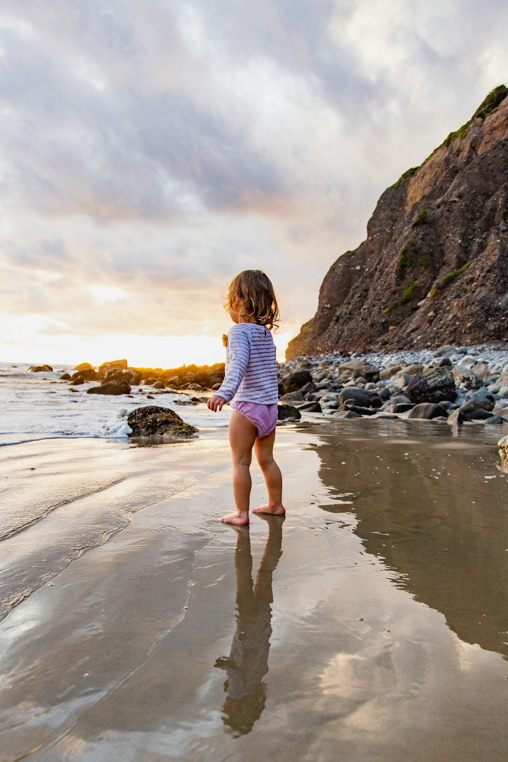 girl in pink and white stripe shirt and blue denim shorts walking on seashore during daytime