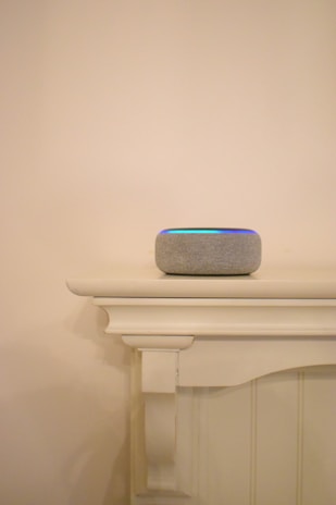 A sleek smart speaker sitting on a modern shelf with soft daylight filtering through nearby curtains.