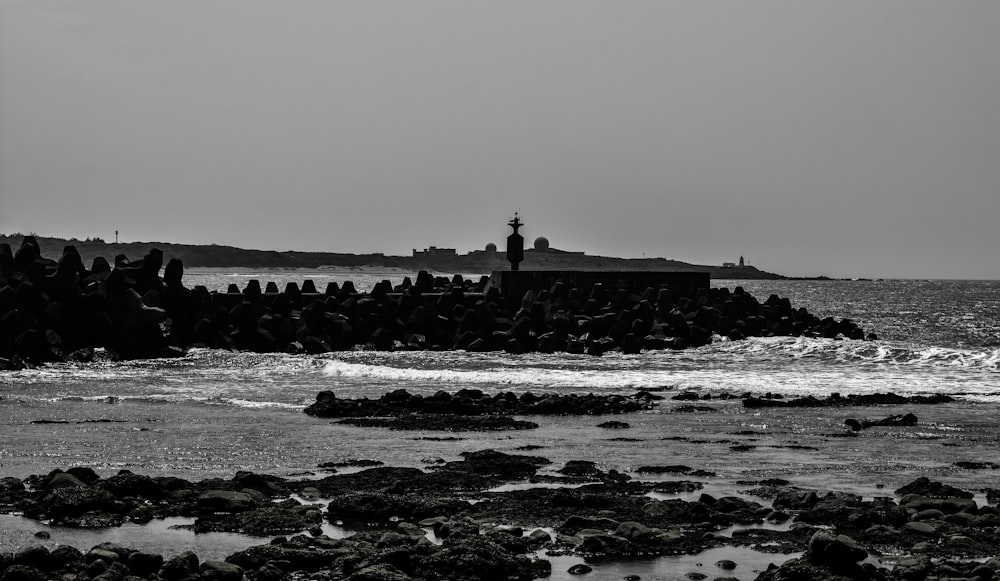 grayscale photo of person standing on rock formation near body of water