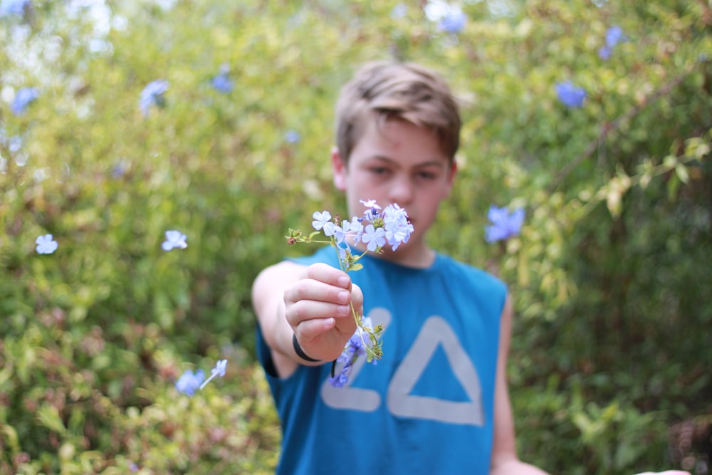 boy in blue crew neck t-shirt holding yellow and purple flower
