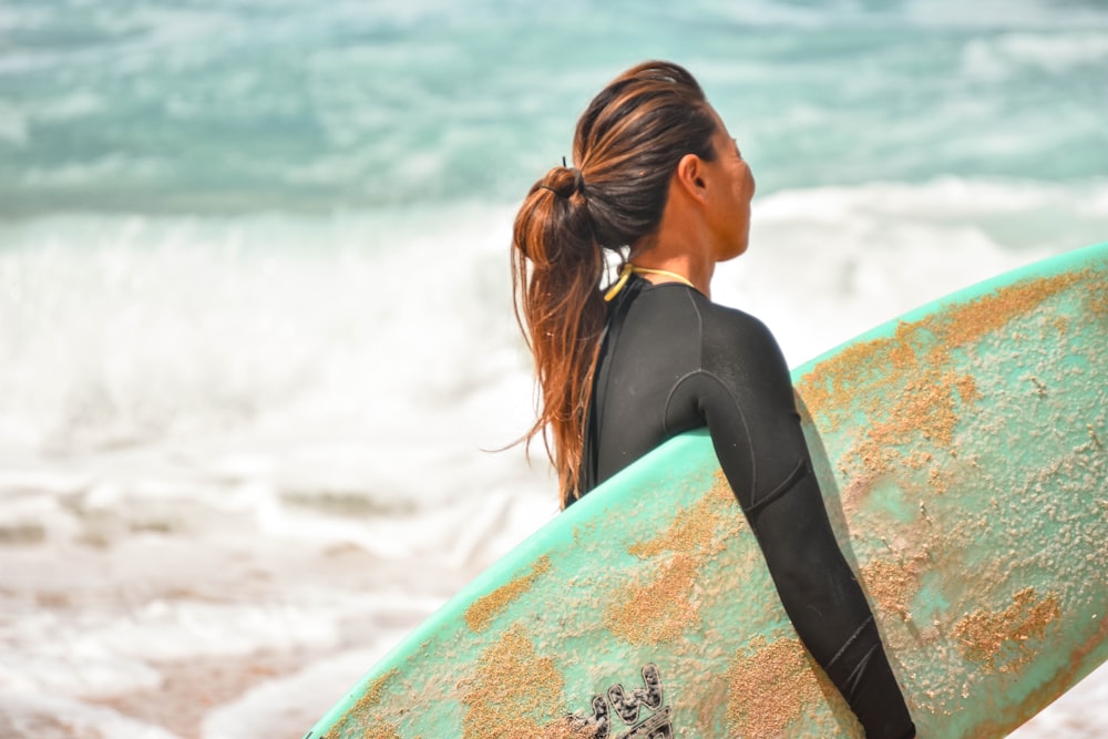 woman in black tank top leaning on blue and orange surfboard during daytime