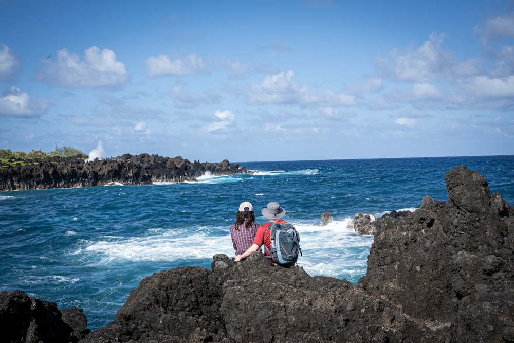 man in red shirt sitting on rock formation near sea during daytime