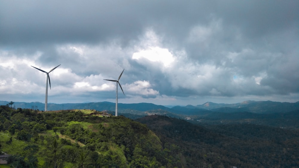 white wind turbine on green mountain under white clouds during daytime