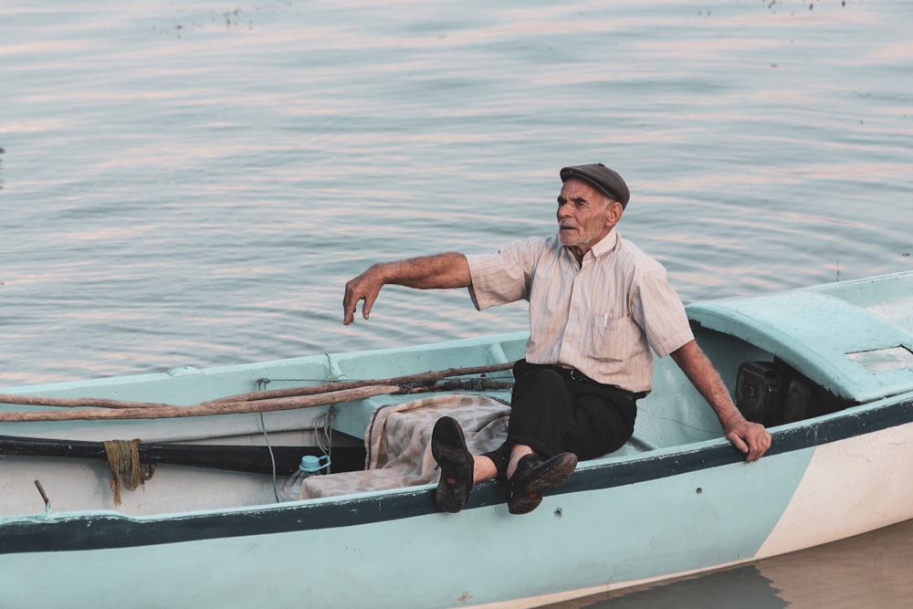 uomo in camicia bianca e pantaloni neri seduto sulla barca bianca e marrone durante il giorno