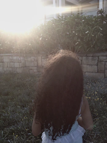 Child playing in a sunlit garden surrounded by soft sand-colored walls and blooming flowers.