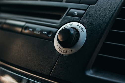 Close-up of a hand tuning a sleek car radio displaying the audioxm interface.