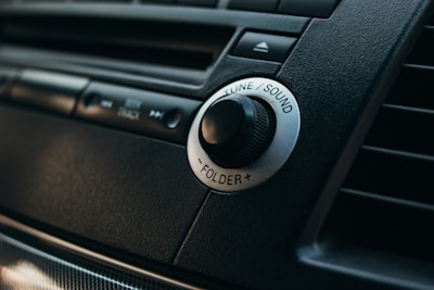 Close-up of a car stereo system focusing on a knob labeled 'Tune/Sound' surrounded by buttons and a dark, textured dashboard.