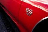 A close-up view of the side of a red car displaying chrome 'SS 454' badging, reflecting light and casting soft highlights.