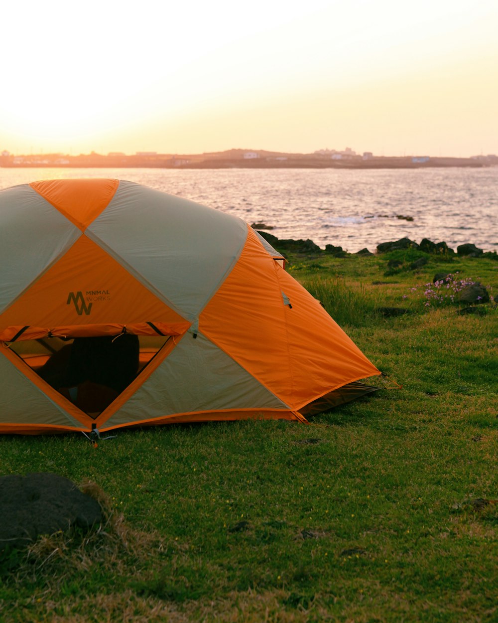 orange and gray dome tent on green grass field near body of water during daytime