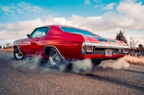 red chevrolet camaro on gray asphalt road under blue and white sunny cloudy sky during daytime