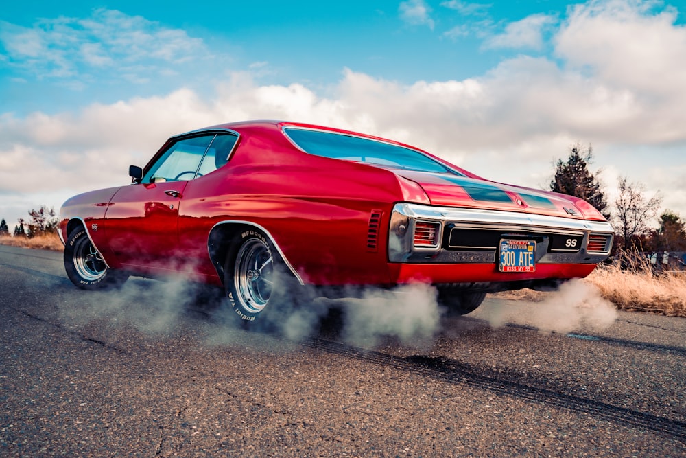 Chevrolet Camaro rouge sur route asphaltée grise sous ciel nuageux ensoleillé bleu et blanc pendant la journée