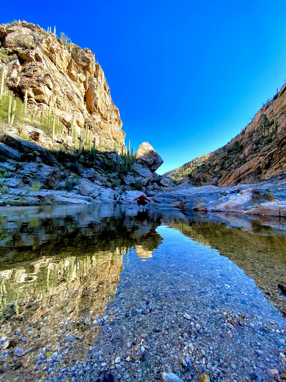 brown rocky mountain beside lake under blue sky during daytime