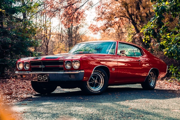 A black 1970 Chevelle SS cruising down a tree-lined country road with autumn leaves.