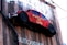 A red vintage car is mounted vertically on a wooden wall with the text 'Mechanic on Duty' displayed on the side. The car appears weathered, adding a rustic charm to the installation. The wall features additional text below, partially visible, displaying 'AUTO REPAIR'.