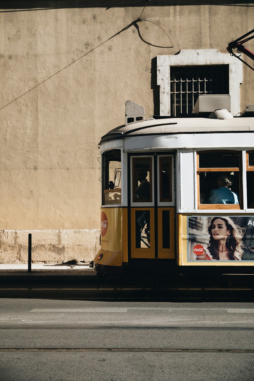 yellow and white tram beside beige concrete wall