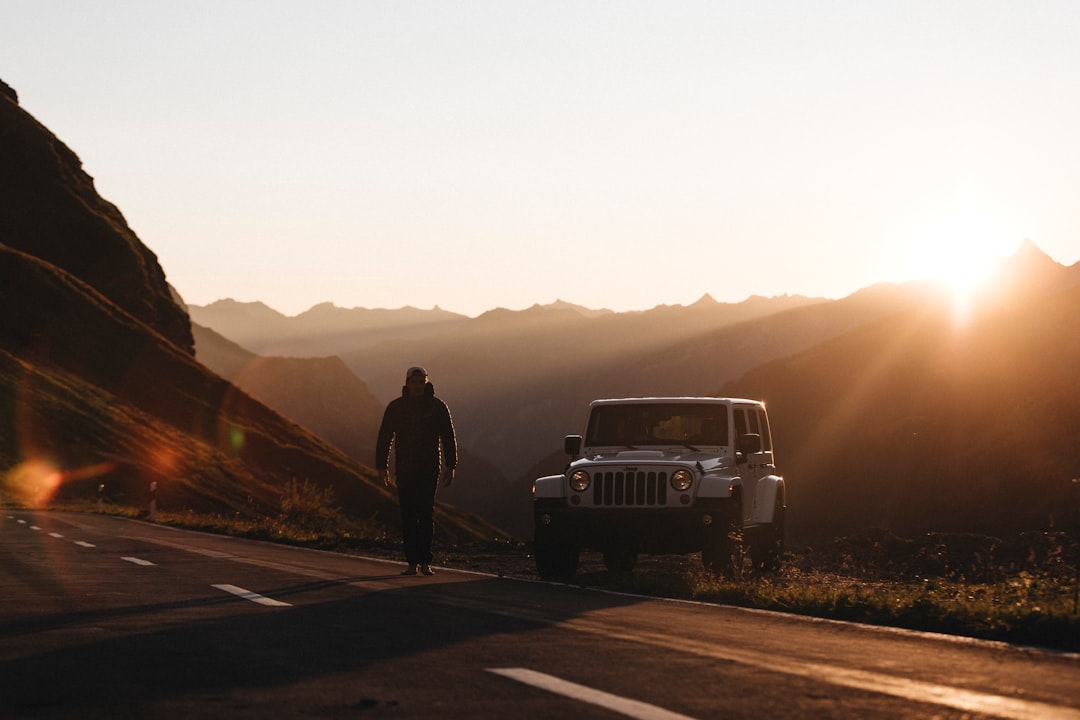 man in black jacket standing beside white suv during daytime