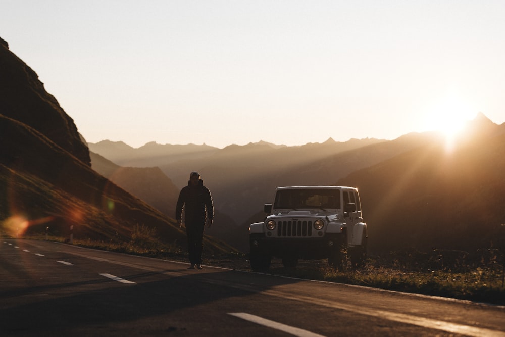 man in black jacket standing beside white suv during daytime