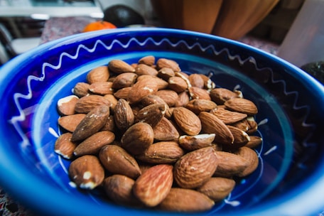 Close-up of glossy almonds spilling from a rustic wooden bowl.