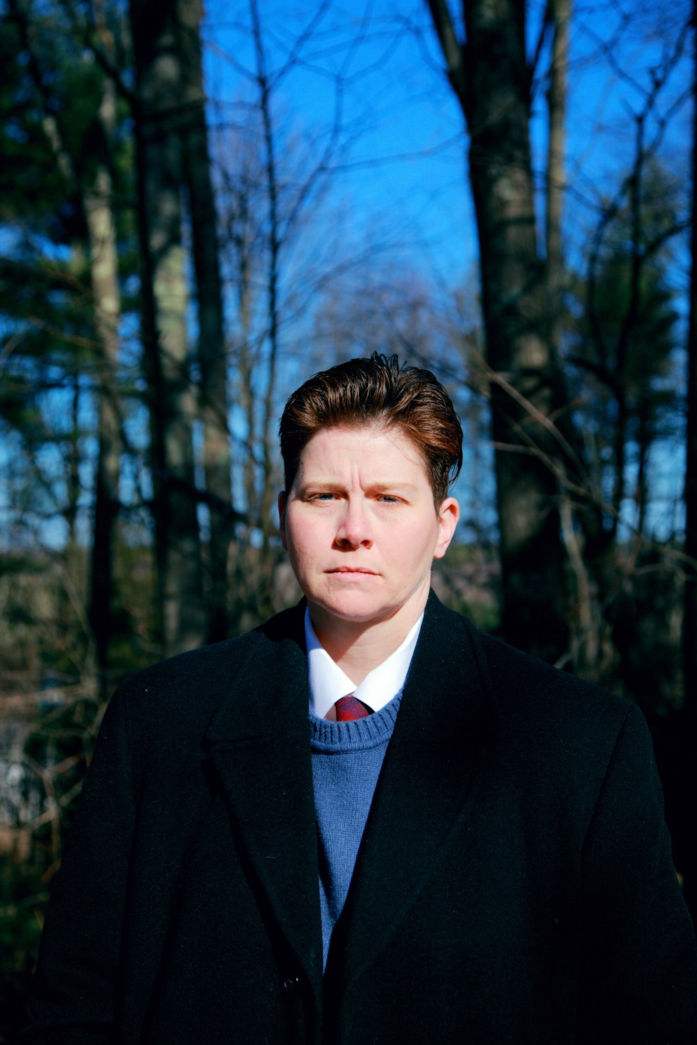 man in black suit jacket standing near trees during daytime