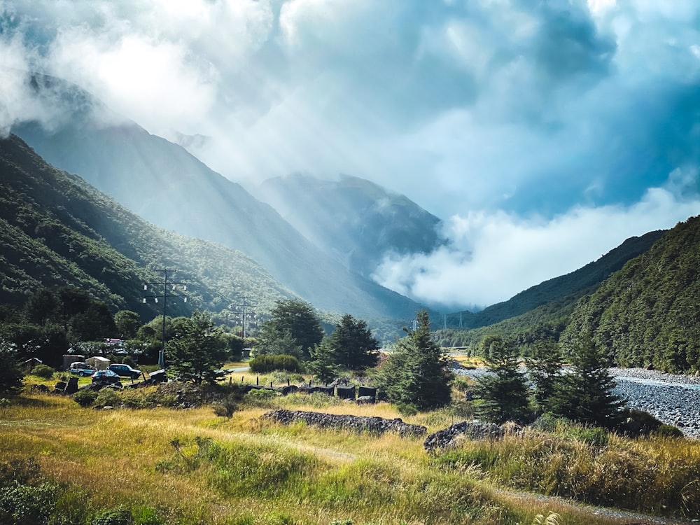 green grass field near mountain under white clouds during daytime