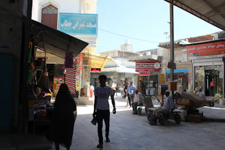 A busy marketplace with diverse people engaging in trade and services under bright daylight.