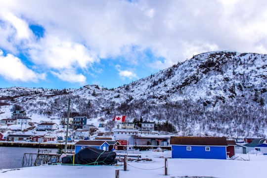 white and blue house near mountain under white clouds during daytime in Petty Harbour Canada