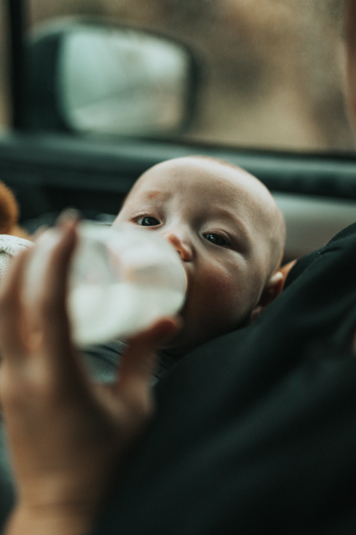 Baby in a blue outfit drinking milk from a feeding bottle